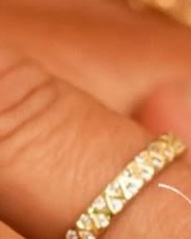 Anel dourado meia aliança com fileira de zircônias, na mão