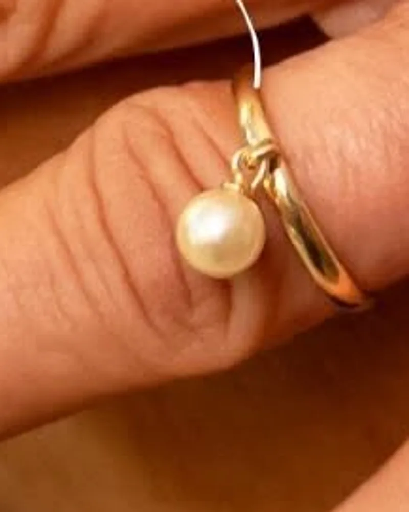 Anel dourado liso com uma pérola pendurada por uma argola