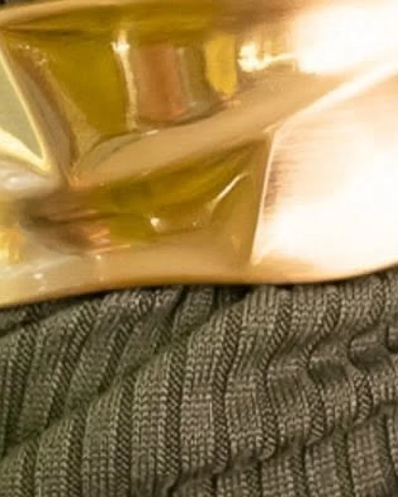 Bracelete dourado largo com superfície ondulada, sobre a manga de uma blusa verde