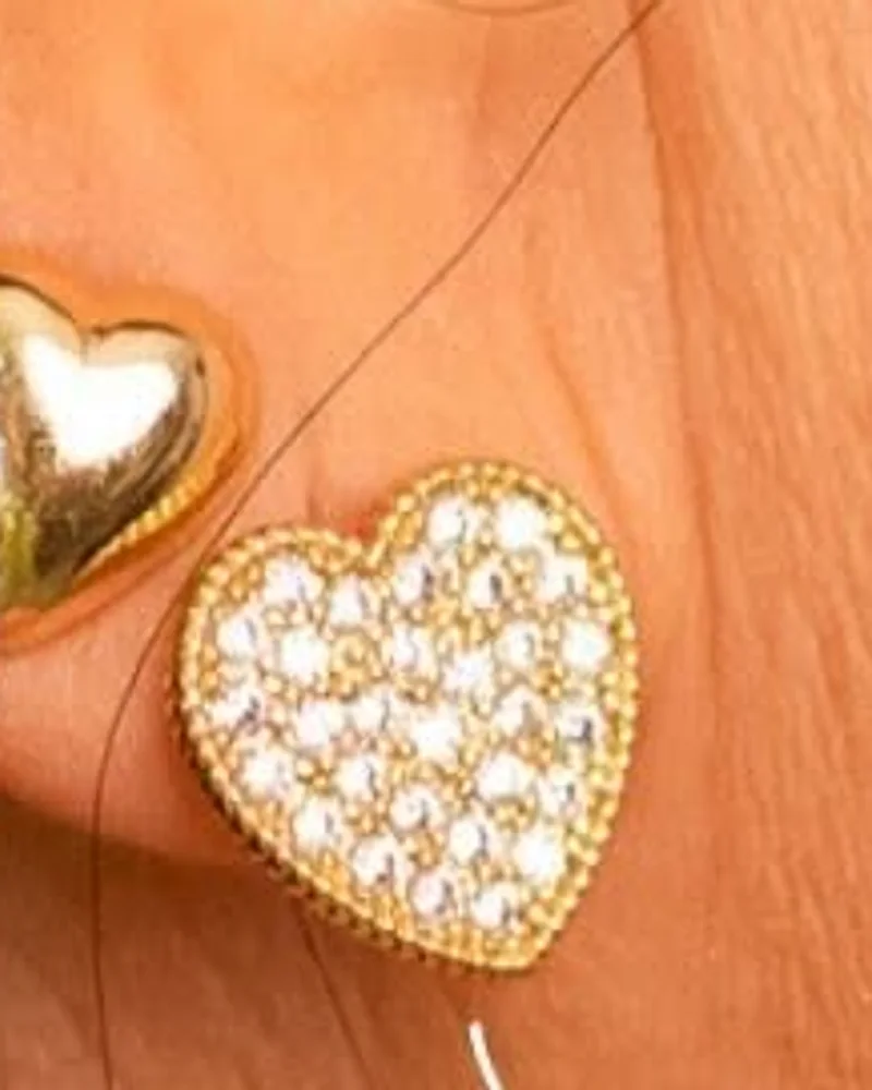 Brinco de coração dourado cravejado de zircônias, visto de perto na orelha