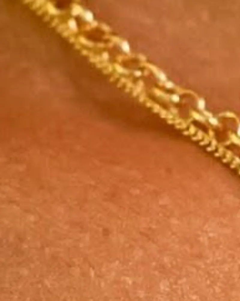 Colar de elo português dourado, de elos redondos, apoiado no colo