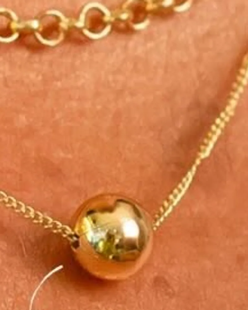Colar dourado fino com pingente de esfera lisa no centro do colo