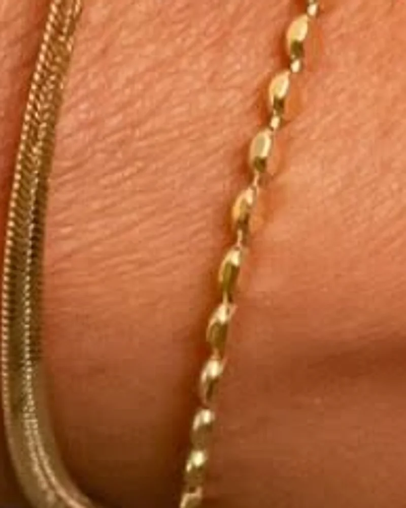 Pulseira dourada de elos facetados no pulso, ao lado de uma segunda pulseira lisa