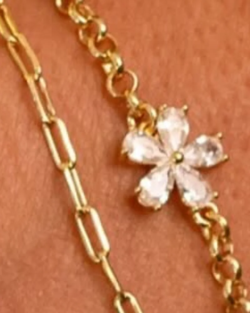 Pulseira dourada com flor de zircônias no centro, ao lado de uma pulseira de elos alongados